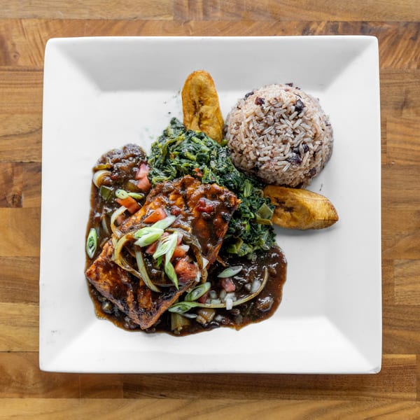Grilled salmon with dark sauce, rice and beans, sauteed greens, and fried plantains on a white plate.