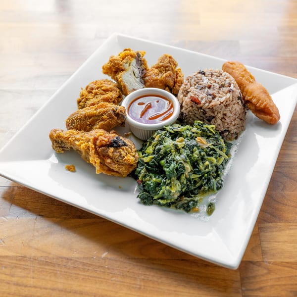 A white plate holds fried chicken, rice and peas, steamed callaloo, and a fried dumpling.