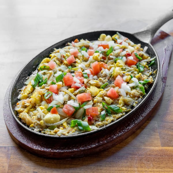 Sizzling sisig, a Filipino dish, served in a hot cast iron skillet on a wooden board.