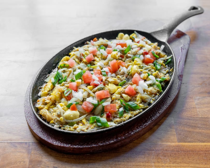 Sizzling sisig, a Filipino dish, served in a hot cast iron skillet on a wooden board.