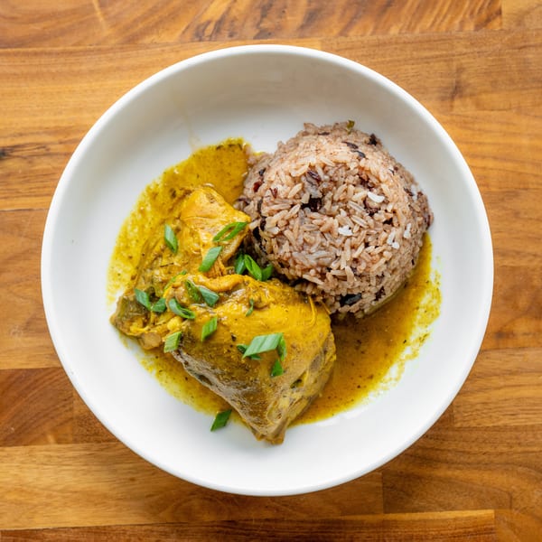 Curried chicken with rice and beans, garnished with green onions, in a white bowl on a wooden table.