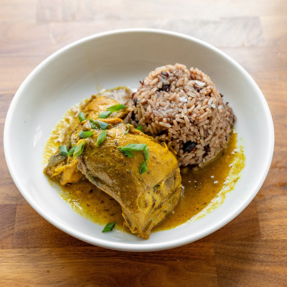 Curried chicken with rice and beans, garnished with green onions in a white bowl.