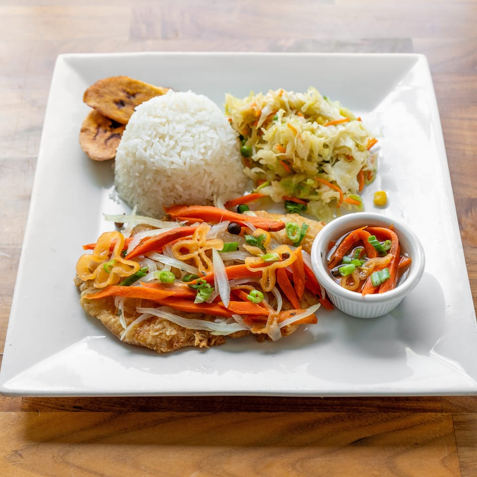 Fried fish topped with pickled carrots and onions, served with rice, coleslaw, and plantains.