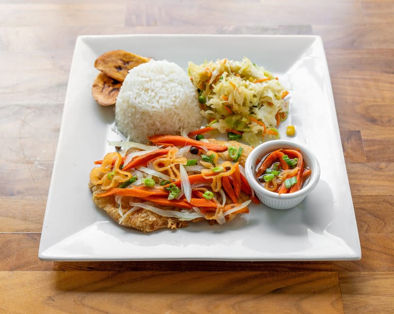 Fried fish topped with pickled carrots and onions, served with rice, coleslaw, and plantains.