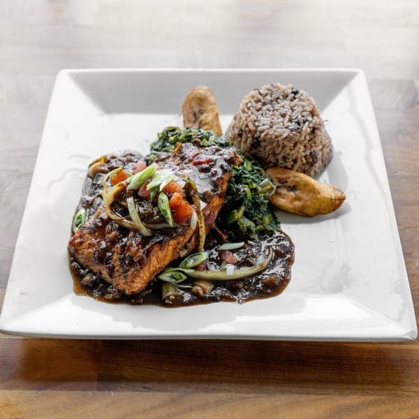 Grilled salmon with dark sauce, rice, greens, and plantains on a white plate.