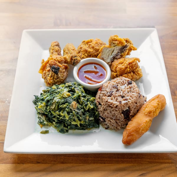 Fried chicken, rice and beans, cooked greens, and a fried plantain on a white plate.