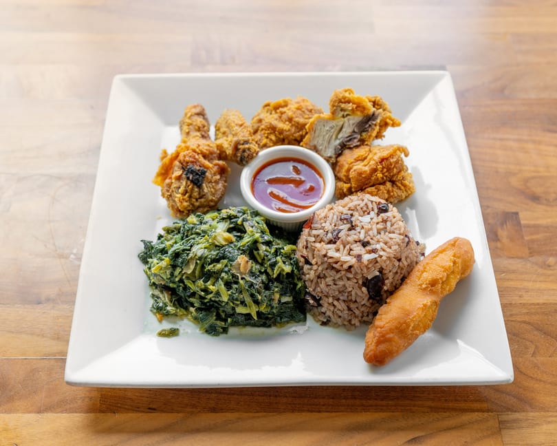 Fried chicken, rice and beans, cooked greens, and a fried plantain on a white plate.