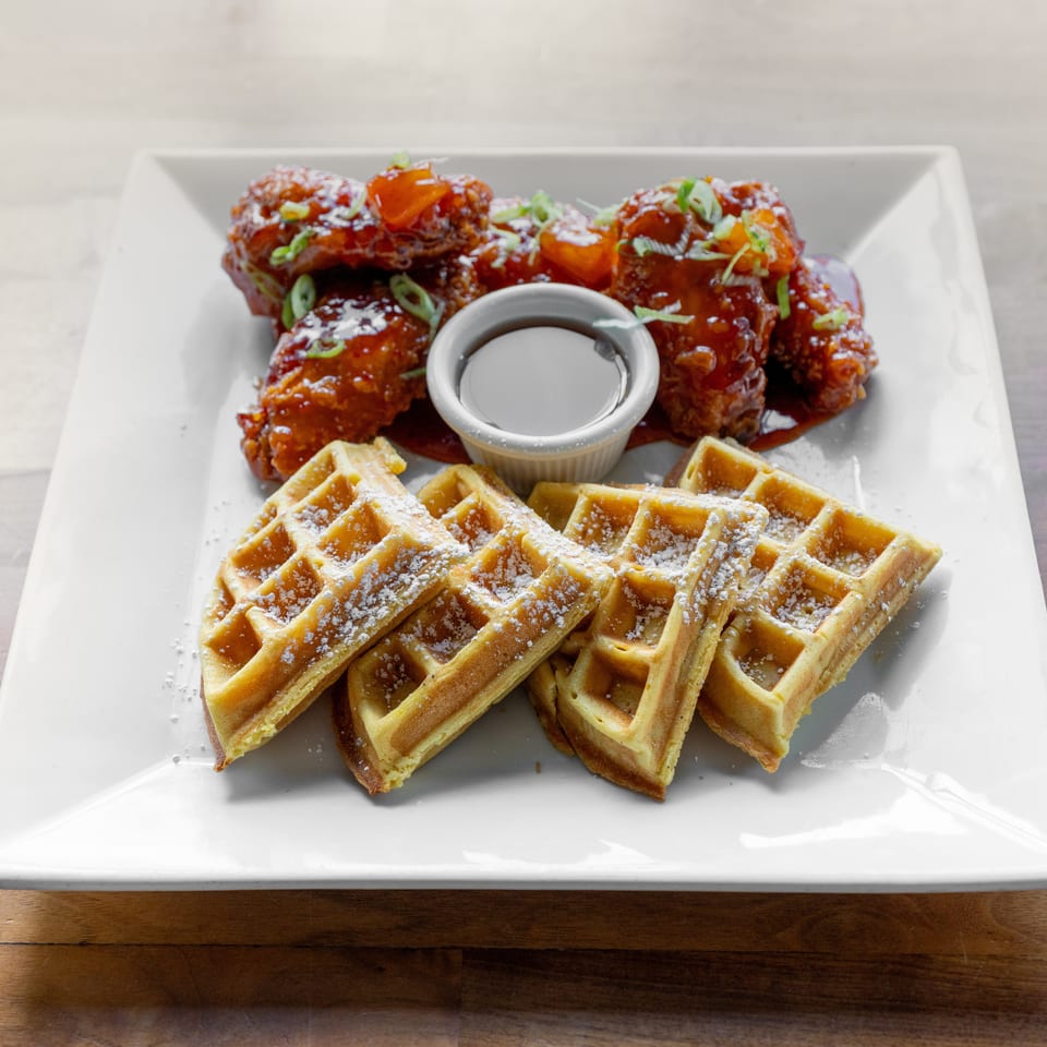 Chicken and waffles dish with crispy chicken wings, syrup, and powdered sugar dusted waffles.