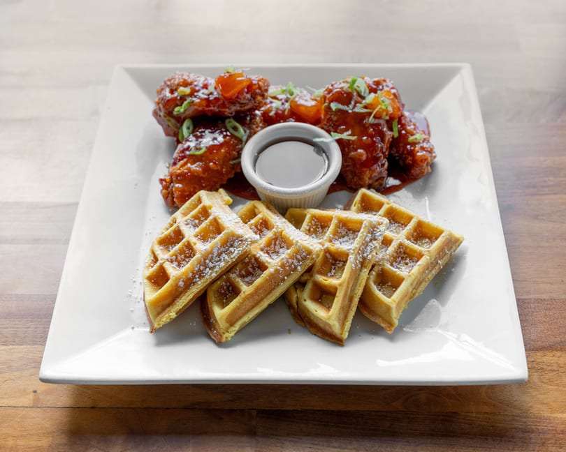 Chicken and waffles dish with crispy chicken wings, syrup, and powdered sugar dusted waffles.