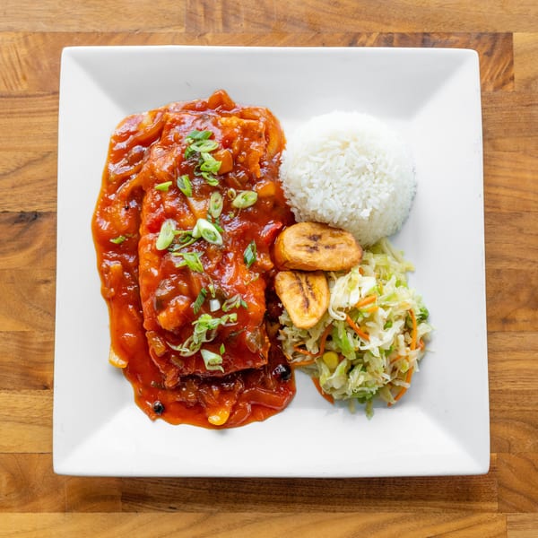 A white plate with fish in red sauce, white rice, fried plantains, and coleslaw.