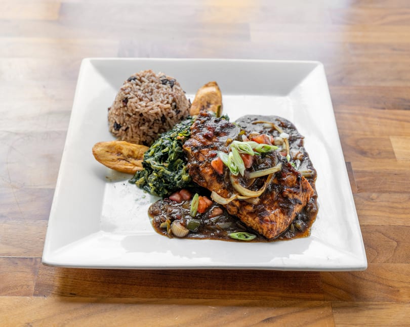 Grilled salmon with dark sauce, rice and beans, sauteed greens, and plantains on a white plate.