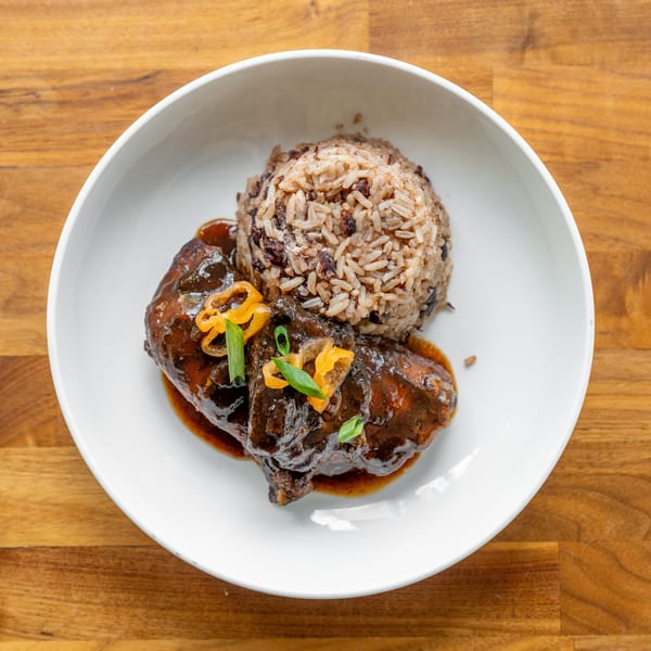 Braised chicken with rice and beans, garnished with peppers and scallions, in a white bowl.