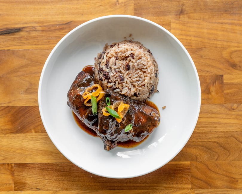 Braised chicken with rice and beans, garnished with peppers and scallions, in a white bowl.