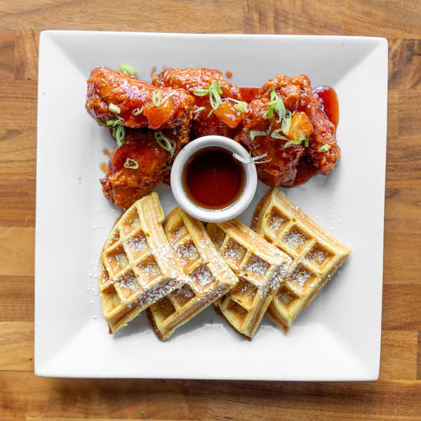 Chicken and waffles with syrup, garnished with green onions and diced fruit on a white plate.