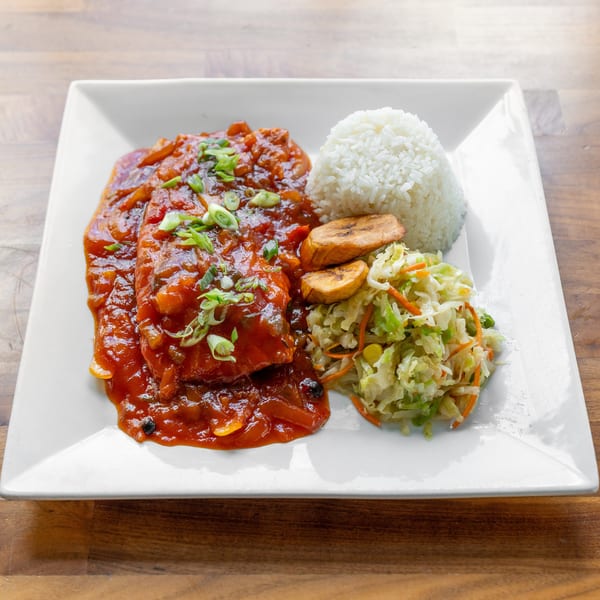 Two pieces of fish in red sauce with rice, fried plantains, and coleslaw on a white plate.