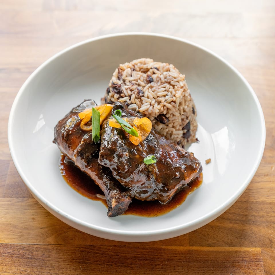 Braised short ribs with dark sauce, garnished with peppers and scallions, served with rice and beans.