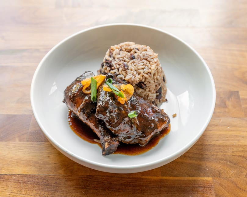 Braised short ribs with dark sauce, garnished with peppers and scallions, served with rice and beans.