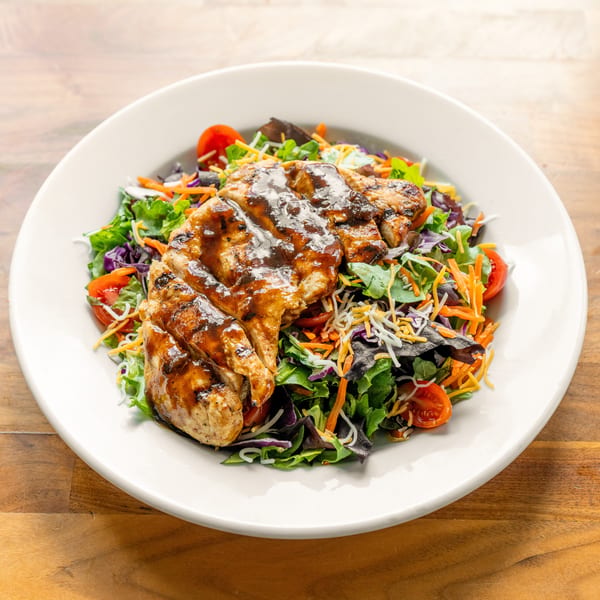 Grilled chicken breast with barbecue sauce on a fresh garden salad with shredded cheese and tomatoes.