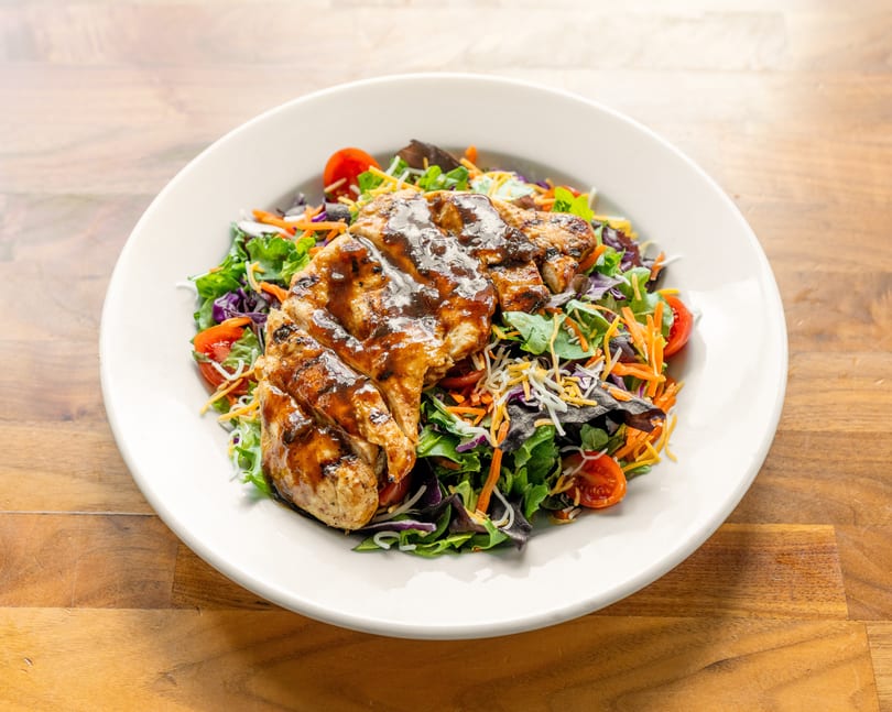 Grilled chicken breast with barbecue sauce on a fresh garden salad with shredded cheese and tomatoes.